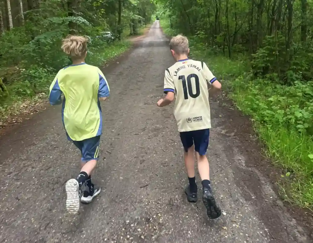 To drenge løber sammen gennem skoven og oplever glæden ved bevægelse og fællesskab.